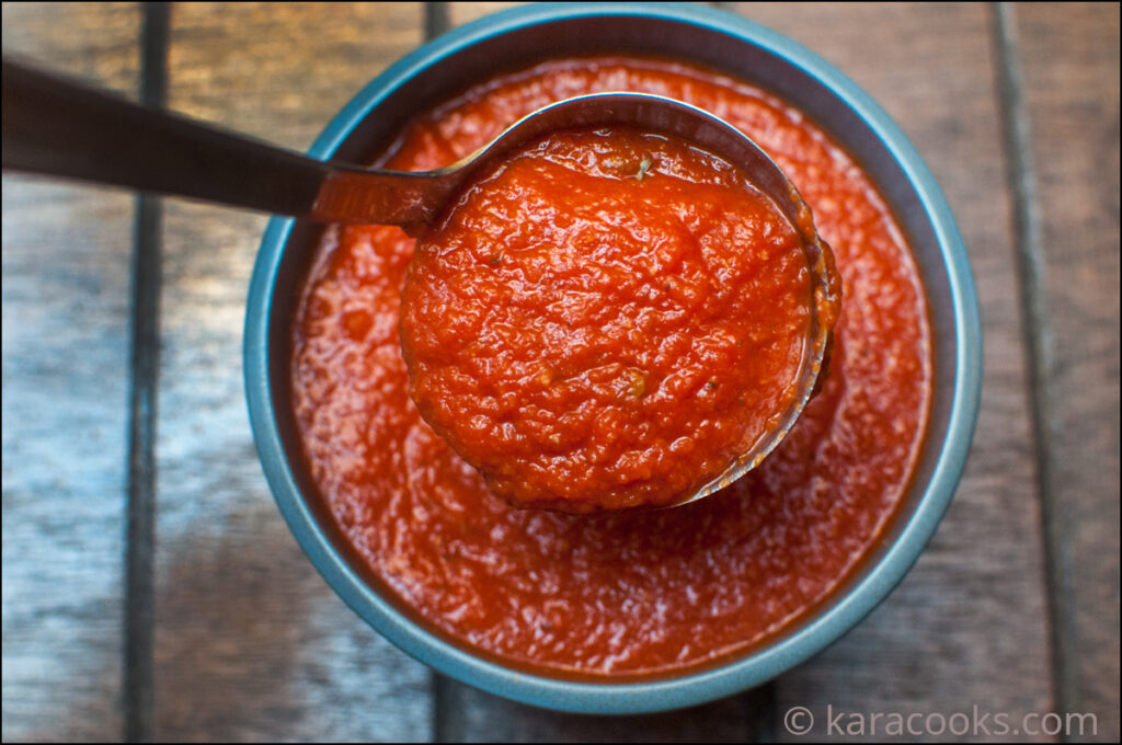 Red tomato sauce in a blue bowl with a ladle full of sauce being spooned out
