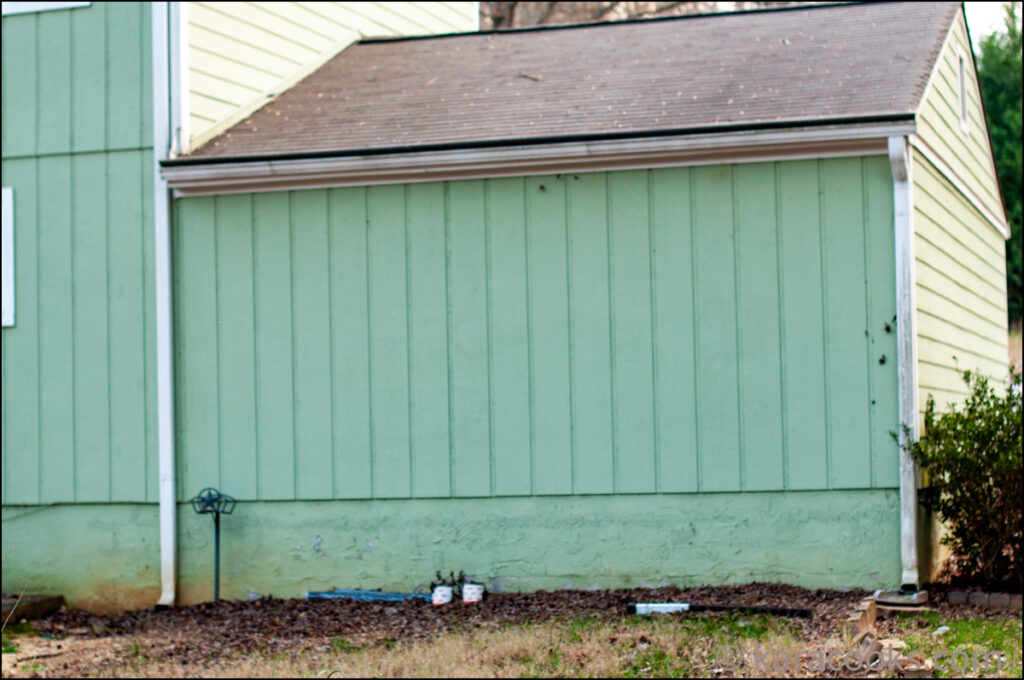 The back of a garage with light green vertical siding and a brown roof