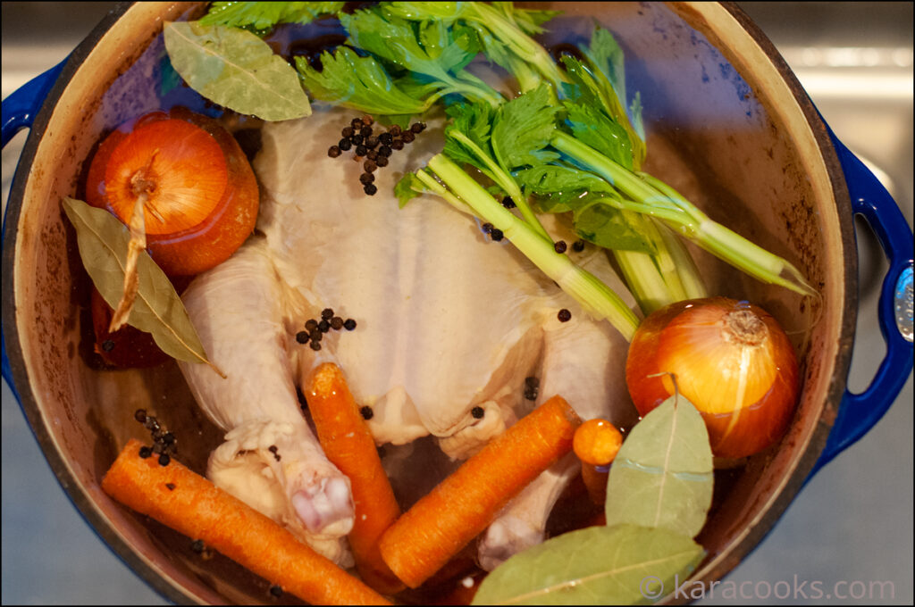 Whole chicken and vegetables in a large stock pot with water